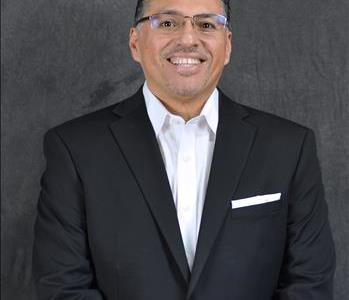 male employee with short black hair, glasses wearing a black suit with a smile
