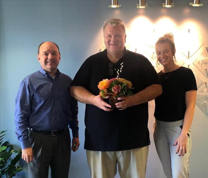 SERVPRO employee delivers a flower bouquet and poses for picture with chamber staff 