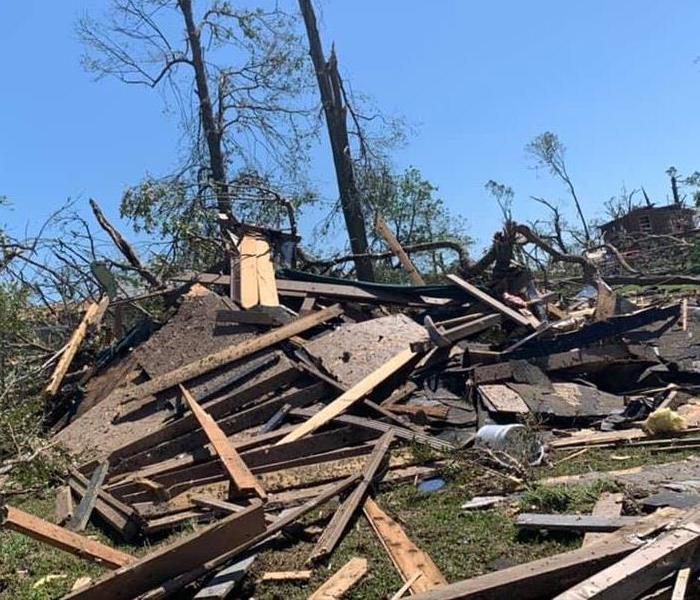 A destroyed house with trees and debris scattered across the home.