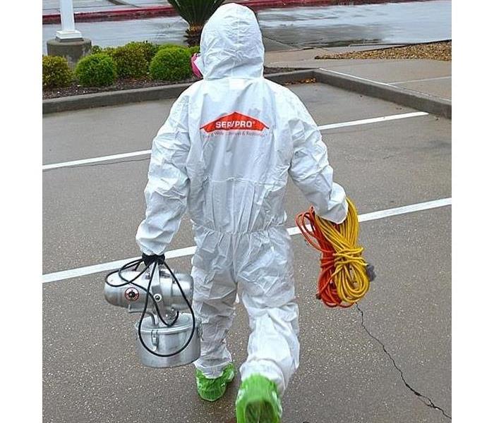 A SERVPRO employee in a TYVEK suit carrying equipment on a site.