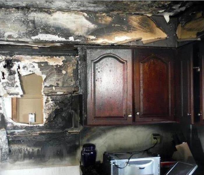 A charred and burned out set of cabinets in a kitchen.